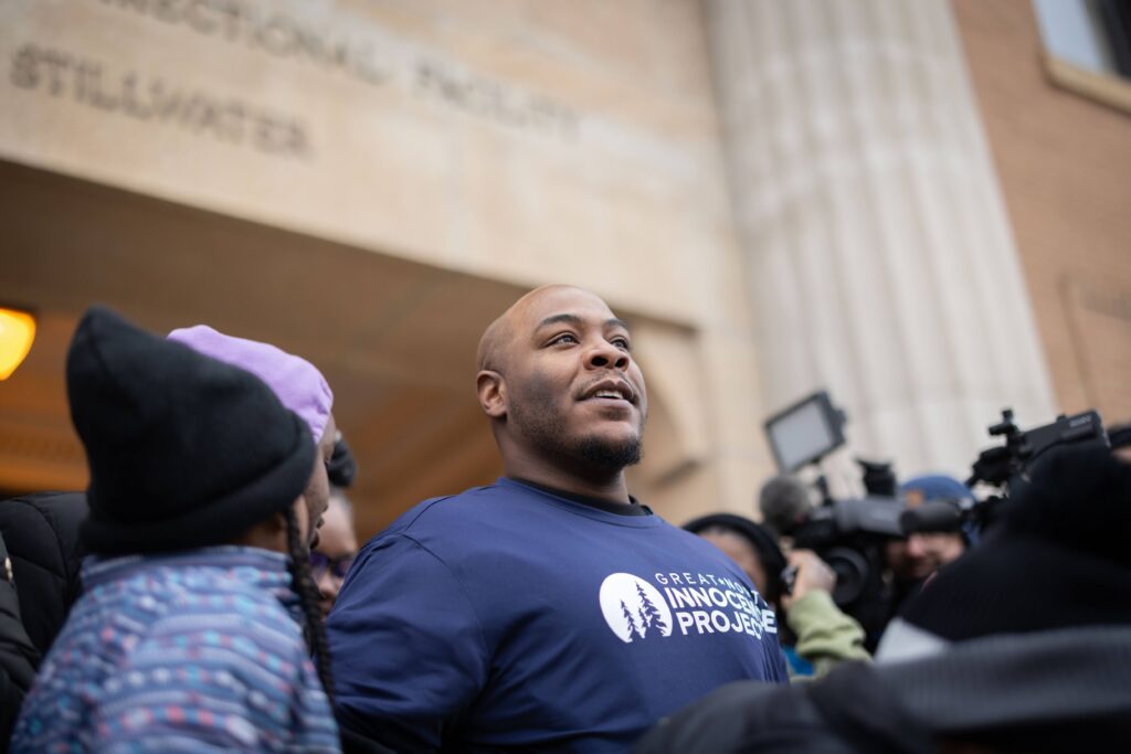 A Black man wears a Great North Innocence Project tee shirt and stands in front of a group of reporters and supporters after being released from prison.