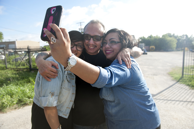 A middle-aged man wearing sunglasses smiles while taking a selfie in between his two adult daughters after release from prison