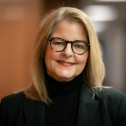 A woman with blonde hair and glasses smiles wearing a black turtleneck
